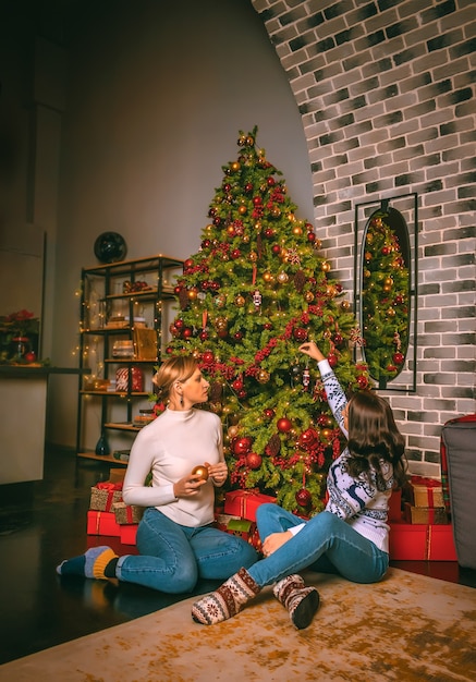 Foto dos mujeres bonitas de cerca bajo el abeto festivo en el interior con las cajas de regalos.