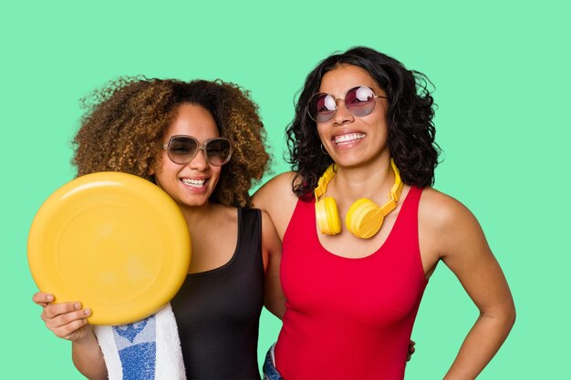 Dos mujeres, una con cabello afro y la otra latina, están listas para unas vacaciones en la playa en traje de baño