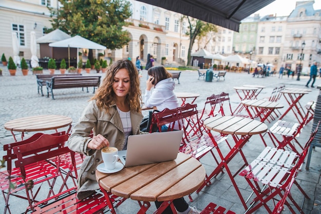 Dos mujeres en un café sentadas en una mesa diferente bebiendo café con leche trabajando en una laptop