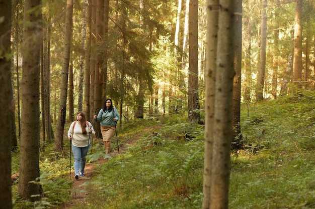 Dos mujeres caminando con palos por el bosque que hacen deporte al aire libre