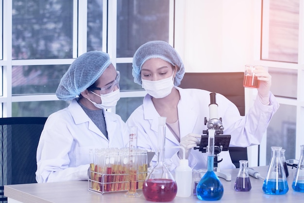 Foto dos mujeres científicas del laboratorio realizan experimentos. el científico jefe de investigación ajusta la muestra en una placa de petri y la observa en el microscopio