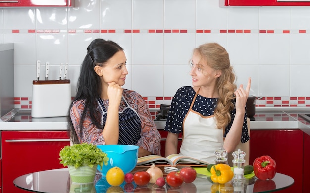 Dos mujeres en la cocina cocinan usando un libro de cocina