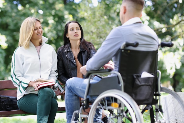 Dos mujeres se comunican con el hombre en el parque en rehabilitación de sillas de ruedas y apoyo de amigos