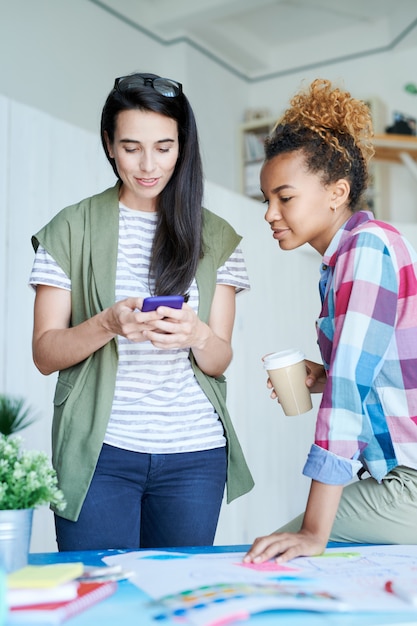 Dos mujeres contemporáneas que usan teléfonos inteligentes en la oficina