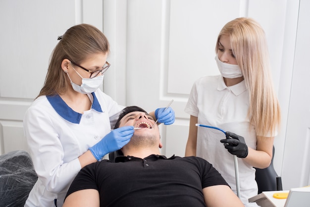 Dos mujeres dentistas revisando los dientes del paciente con herramientas dentales - espejo y sonda en la oficina de la clínica dental. Concepto de medicina, odontología y cuidado de la salud.