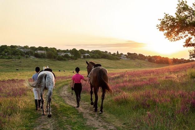 Dos mujeres y dos caballos al aire libre en verano feliz atardecer juntos naturaleza