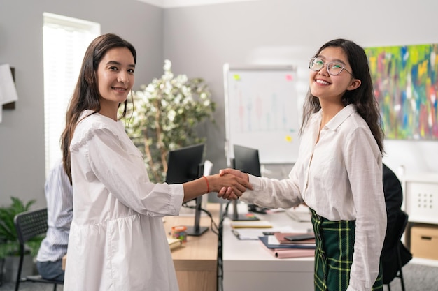 Dos mujeres elegantemente vestidas están de pie en medio de la oficina corporativa y están sonriendo