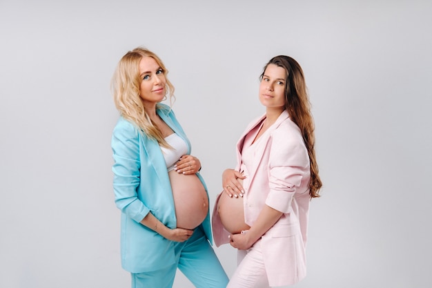 Dos mujeres embarazadas con grandes vientres en trajes sobre un fondo gris.