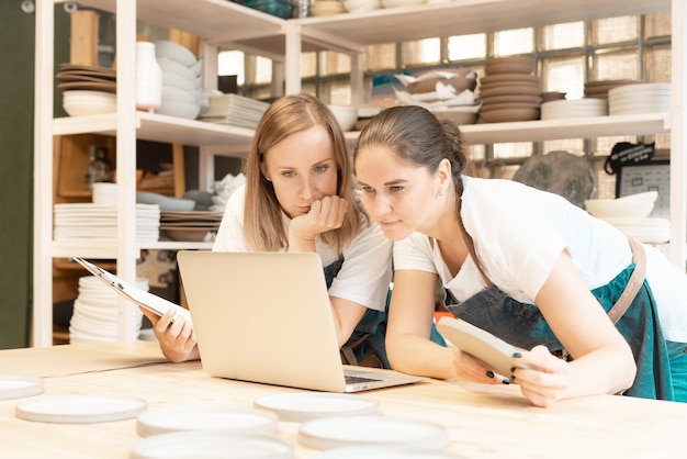 Dos mujeres emprendedoras con laptop en taller artesanal