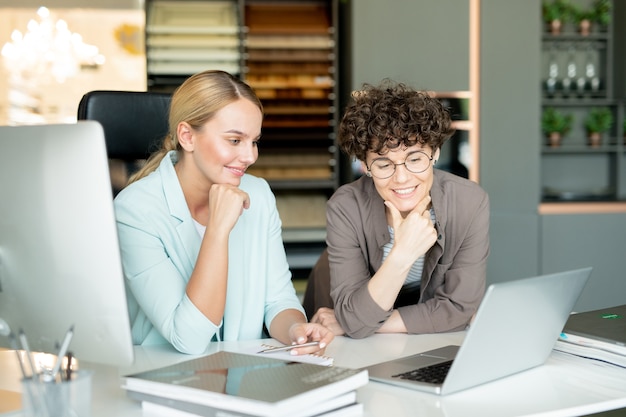 Dos mujeres empresarias mirando atentamente la pantalla del portátil mientras miran un curso en línea para diseñadores