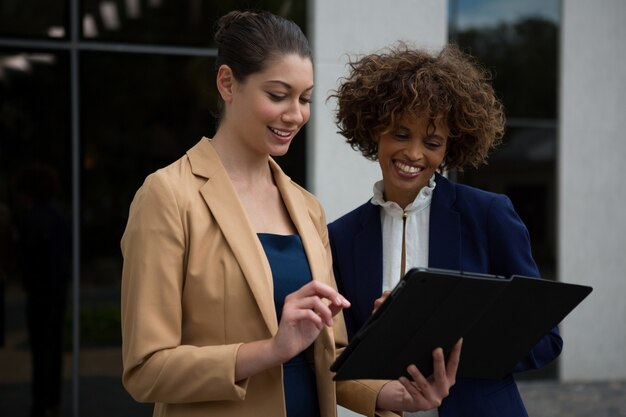 Dos mujeres empresarias con tableta digital cerca del edificio de oficinas