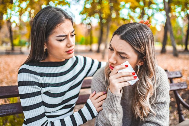 Dos mujeres están sentadas en un banco y se consuelan mutuamente.