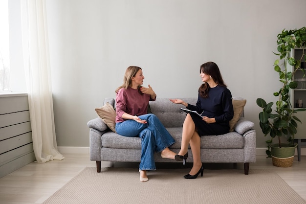 Dos mujeres están sentadas en un sofá en una habitación y hablando. Una conversación sincera. Confía en una persona. amistad femenina