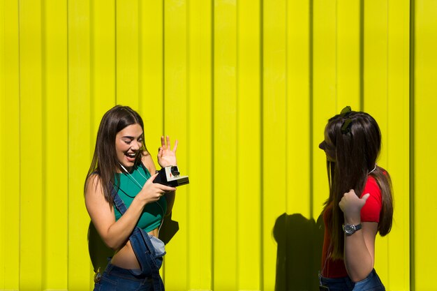 Dos mujeres felices bastante jóvenes tomando fotos con cámara retro y pasar un buen rato