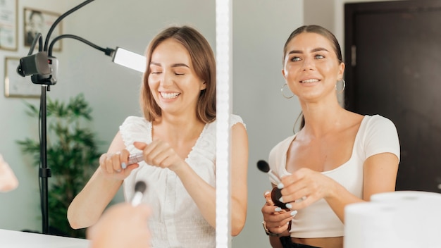 Dos mujeres felices están usando maquillaje mirando en un espejo en un salón de belleza