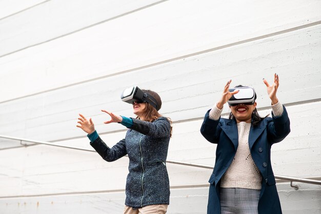 Dos mujeres felices con gafas de realidad virtual se divierten y gesticulan como atrapar algo.