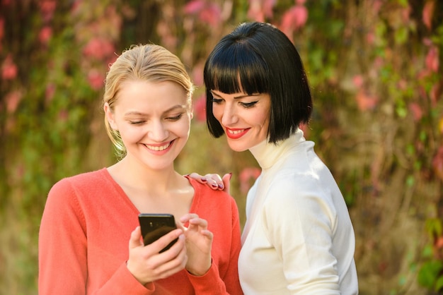 Dos mujeres felices miran en el teléfono nueva tecnología comprar en línea el lunes cibernético viernes negro compras en línea compartir información red social solo mire este marketing digital de navegación por Internet móvil 3g 4g