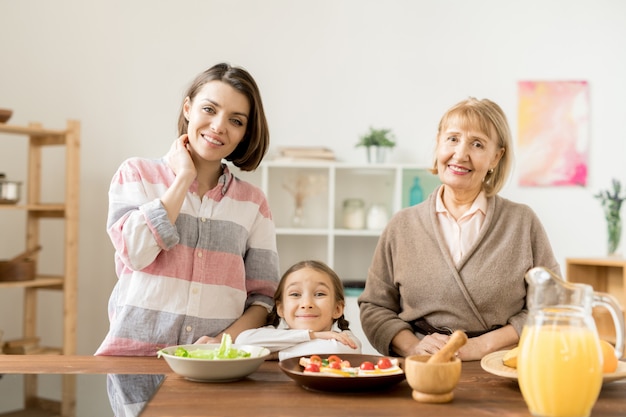 Dos mujeres felices y una niña mirándote mientras vas a preparar una cena festiva y saludable