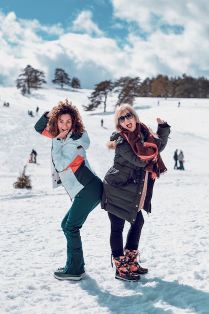 Dos mujeres felices de pie y divirtiéndose en la nieve en el soleado día de invierno.