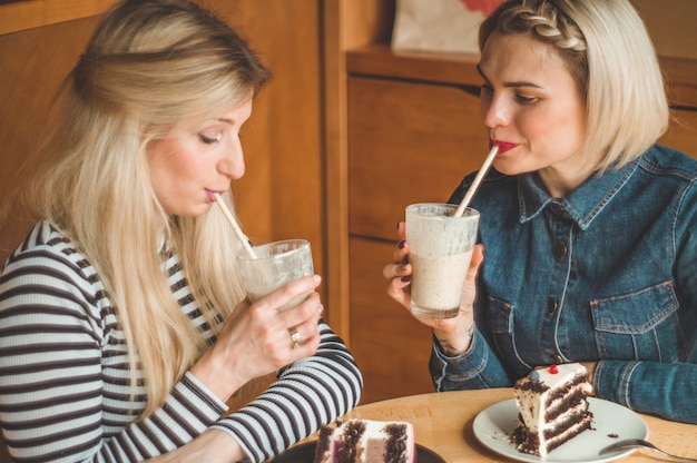 Dos mujeres felices sentadas en un café, beben un cóctel, se cuentan historias divertidas, están de buen humor, riendo felices. Mejores amigos