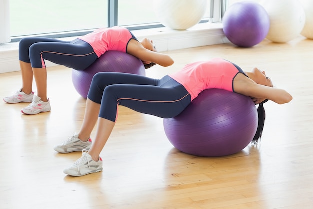 Dos mujeres en forma que se extiende en las bolas de la aptitud en el gimnasio