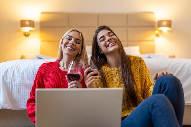 Foto dos mujeres hermosas bebiendo vino y usando la computadora portátil para una llamada de video en línea y brindis en línea con sus amigos fiesta en línea para amigos