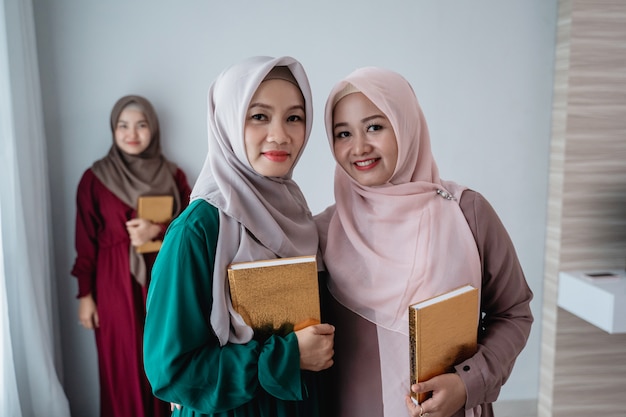 Dos mujeres hijab sonriendo sostienen el libro sagrado de Al-quran