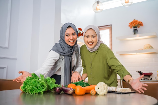 Dos mujeres con hijabs sonríen con las manos en la mesa mientras cocinan en la cocina