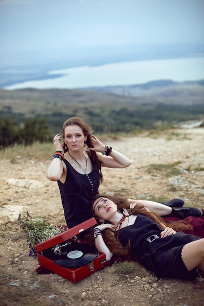 Dos mujeres hippies yacen en un campo en una montaña con un viejo gramófono en un disco de vinilo