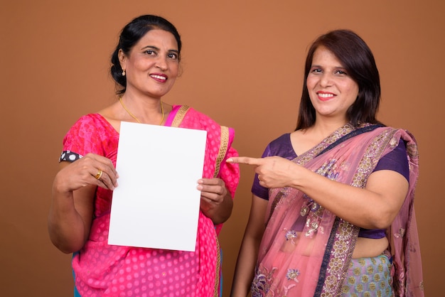 Dos mujeres indias maduras vistiendo ropas tradicionales de la India Sari junto con papel en blanco