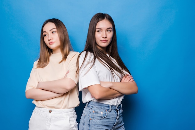 Dos mujeres insatisfechas posando aislado en la pared azul amarillo. Concepto de estilo de vida de personas. Burlarse del espacio de la copia. Tomados de la mano cruzados