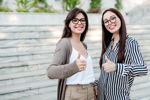 Dos mujeres inteligentes muestran los pulgares al aire libre