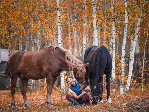 Dos mujeres jinetes se sientan en la hierba junto a los caballos.