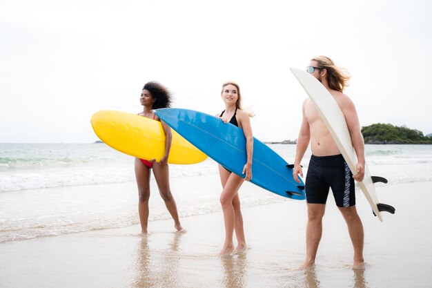 Dos mujeres y un joven con tablas de surf listos para caminar en el mar para surfear