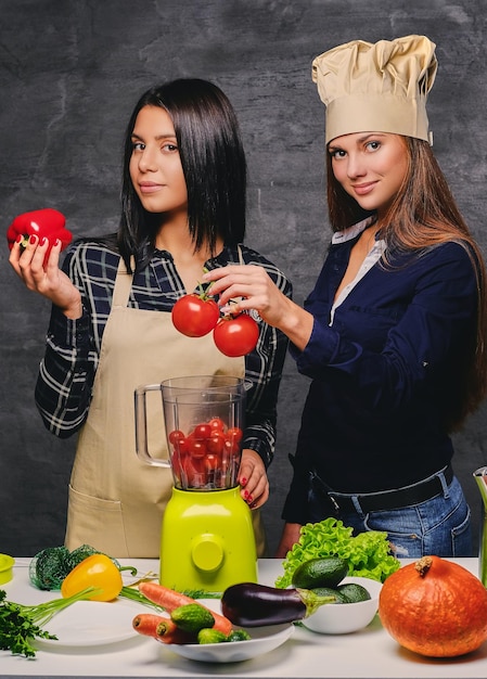 Dos mujeres jóvenes atractivas preparando jugo de vegetales veganos con licuadora.