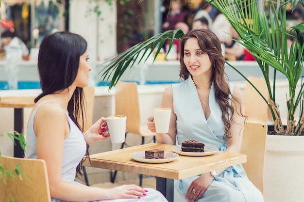 Dos mujeres jóvenes beben café con trozos de tarta en el café al aire libre