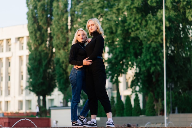 Dos mujeres jóvenes caminando sonriendo abrazándose y besándose al aire libre en la ciudad