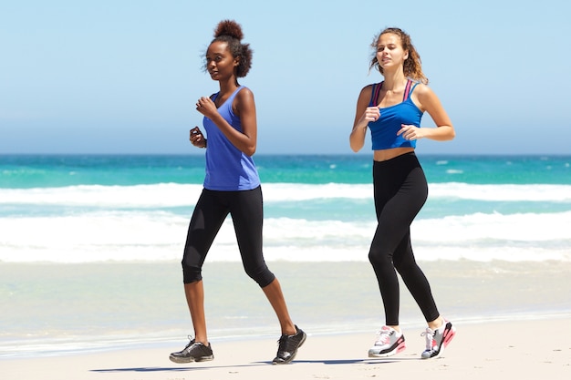 Dos mujeres jóvenes corriendo por el agua en la playa