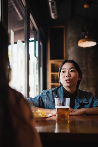 Dos mujeres jóvenes cotilleando mientras están sentadas en un restaurante. Están tomando una cerveza.