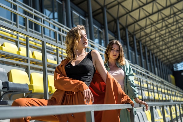 Dos mujeres jóvenes deportivas delgadas se relajan después del ejercicio sentados en los asientos del estadio