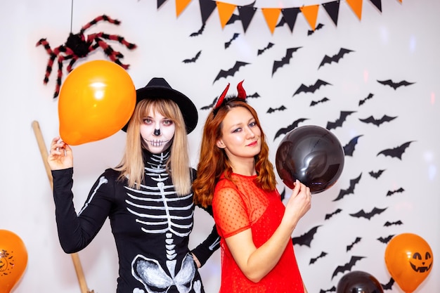 Foto dos mujeres jóvenes con disfraces de carnaval de un esqueleto y un diablo en una fiesta de halloween