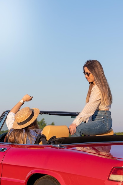 Foto dos mujeres jóvenes disfrutando del tiempo juntas en un coche convertible clásico rojo en vacaciones de verano