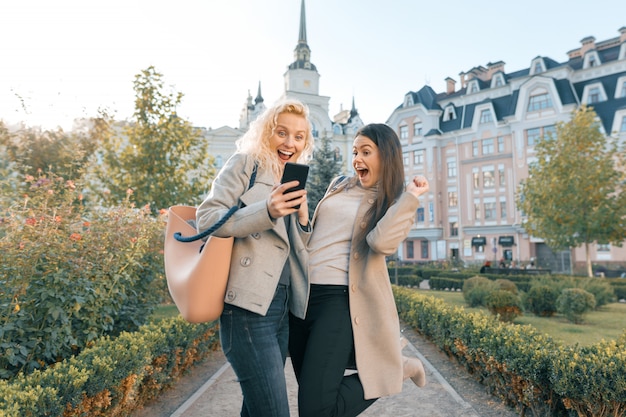 Dos mujeres jóvenes divirtiéndose, mirando el teléfono inteligente riendo