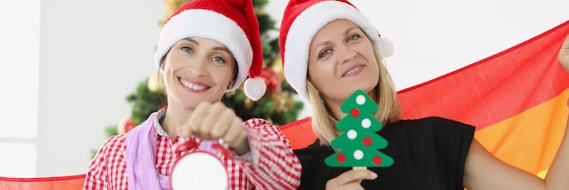 Dos mujeres jóvenes felices con bandera lgbt con árbol de año nuevo y despertador feliz sexual