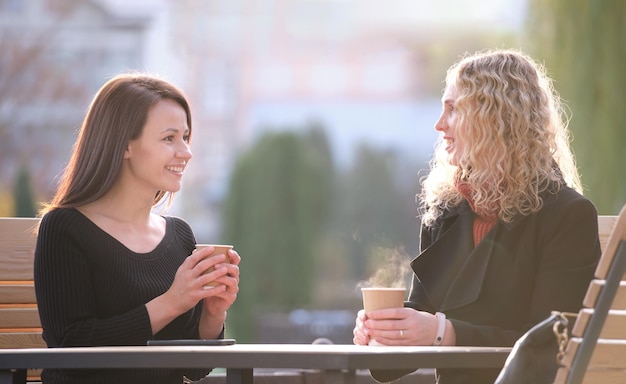 Dos mujeres jóvenes felices sentadas en el café de la calle de la ciudad divirtiéndose juntas durante la pausa para el café