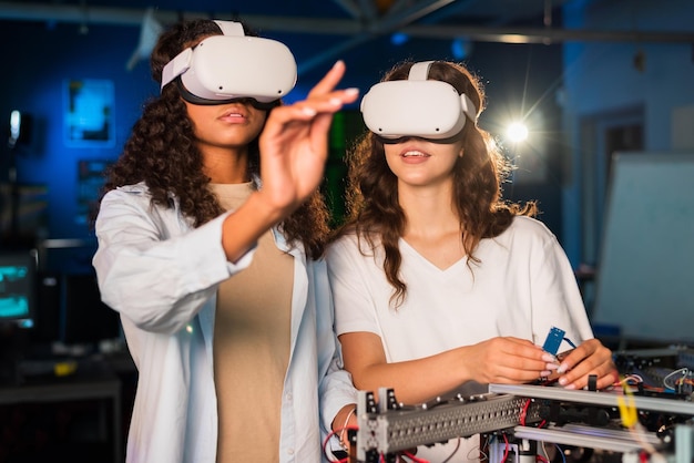 Dos mujeres jóvenes con gafas VR haciendo experimentos en robótica en un laboratorio Robot sobre la mesa