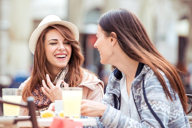 Dos mujeres jóvenes con gran sonrisa y peinado sentadas en un bar.