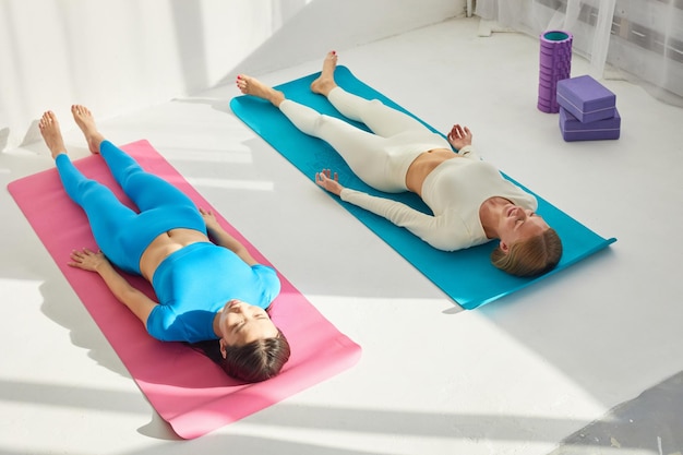 Dos mujeres jóvenes haciendo la postura de savasana después de la clase de yoga