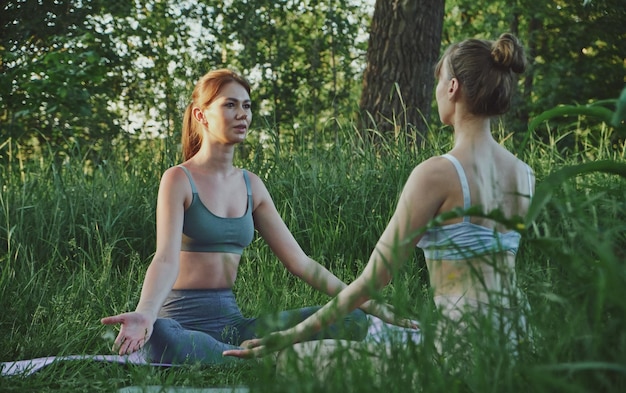 Dos mujeres jóvenes haciendo yoga Padmasana Lotus plantean meditación al aire libre y atención de salud mental