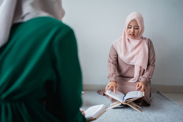 Dos mujeres jóvenes con hiyabs leen juntas el libro sagrado del Al-Quran